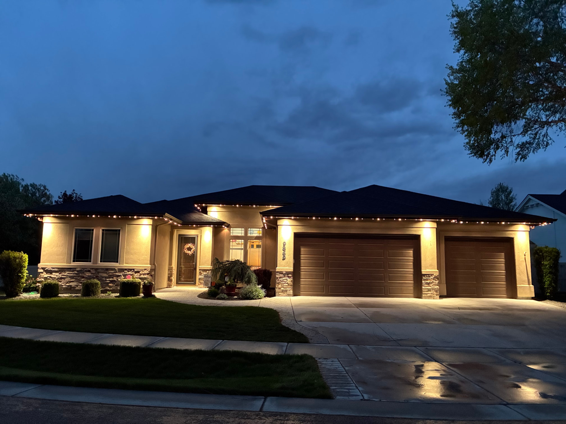 Single-story home at dusk with warm white permanent roofline lighting and stone accents