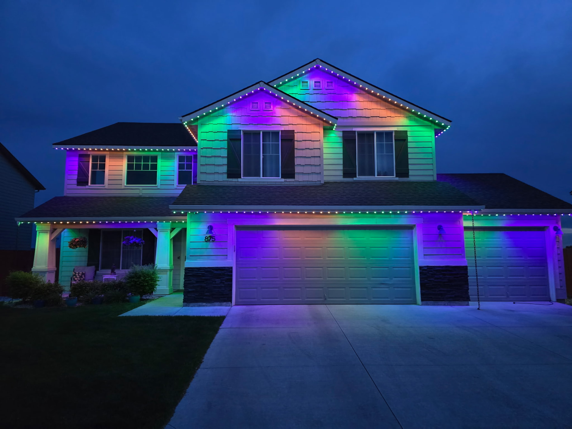 Same two-story home lit in vibrant rainbow colors for a holiday scene