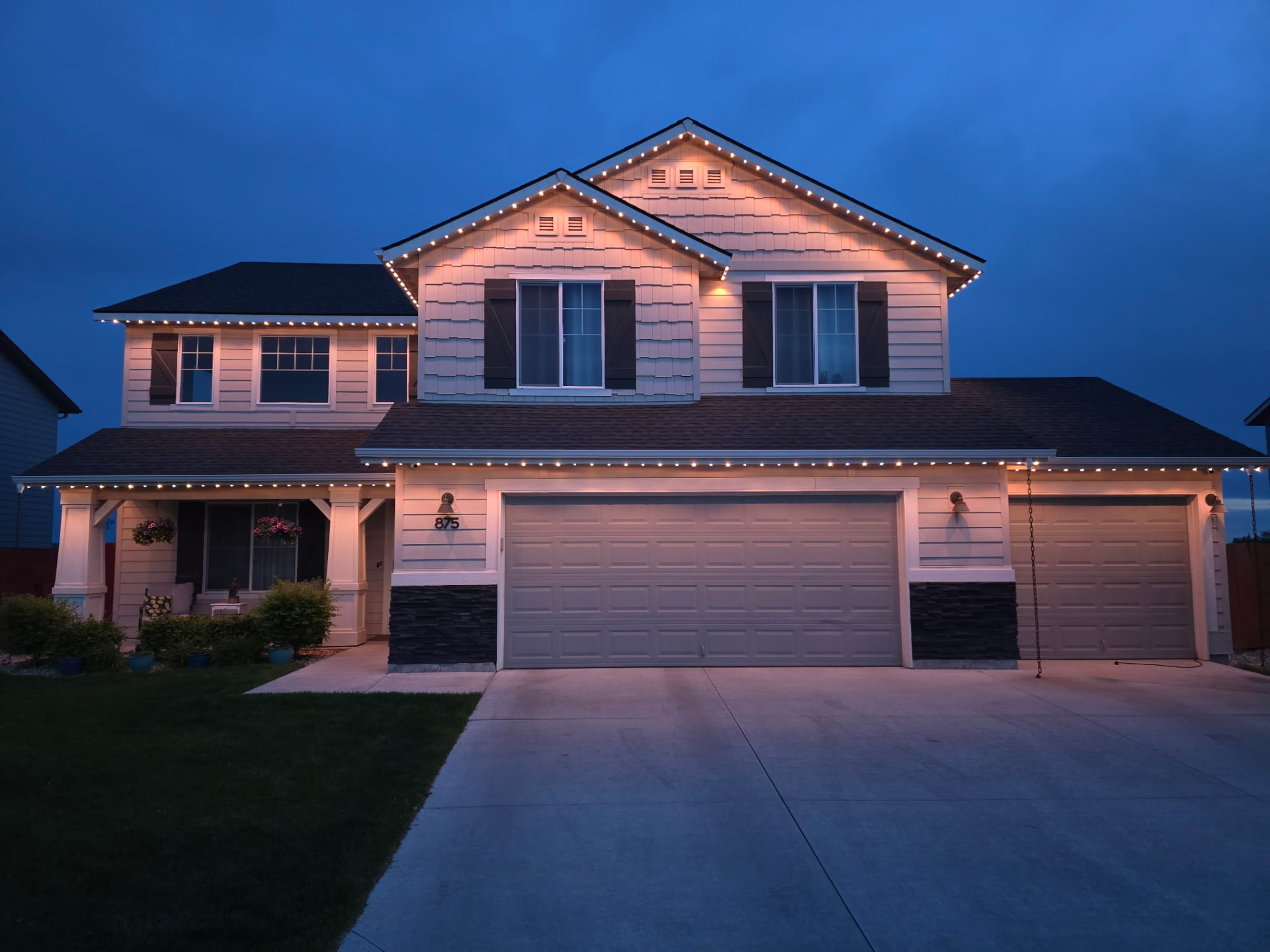 Two-story home with soft warm white permanent roofline lighting against a deep blue evening sky